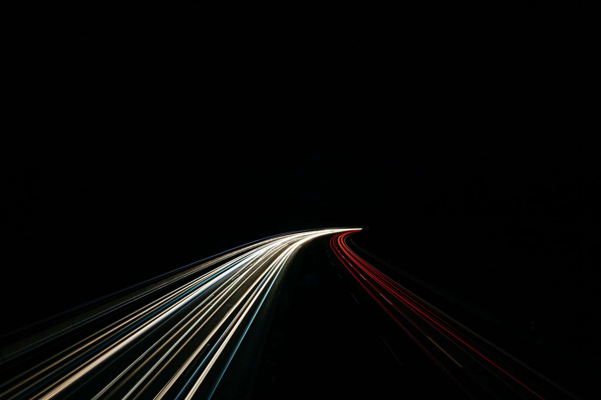 Headlights and tail lights drawn into curving lines along a dark road at night.